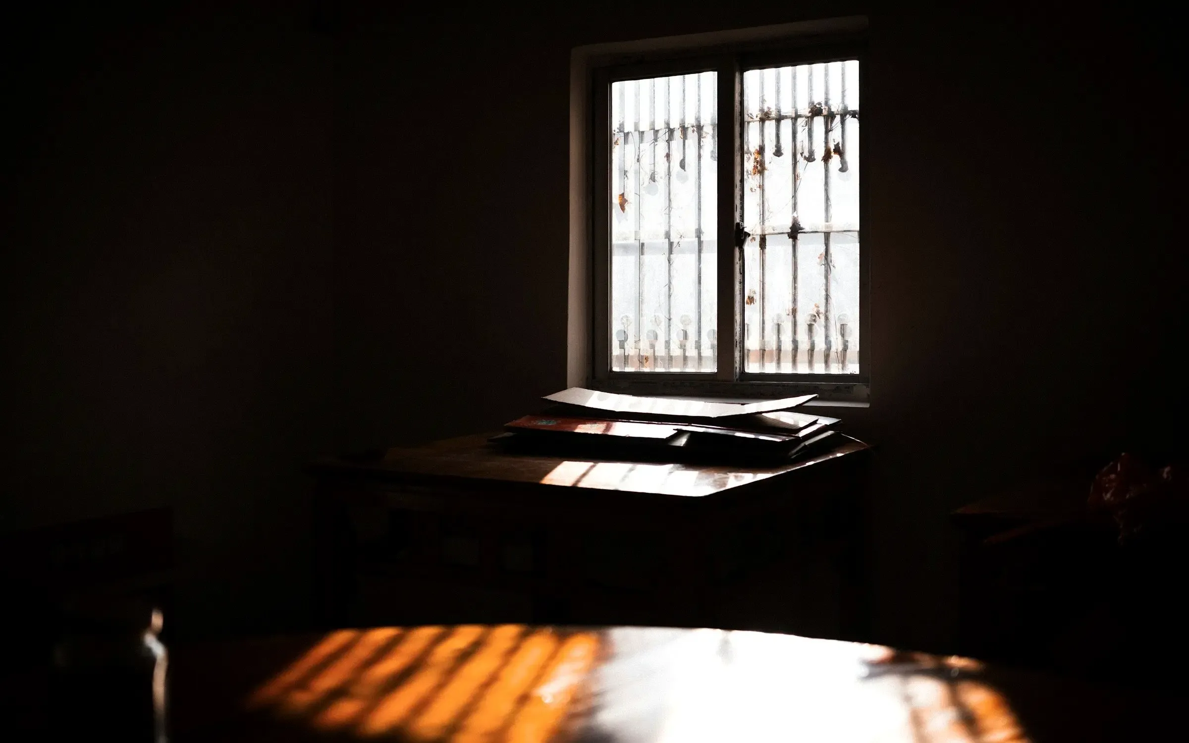 Ein dunkler Raum auf Zypern: durch ein vergittertes Fenster fällt Sonne auf einen Tisch, auf dem Papiere liegen.