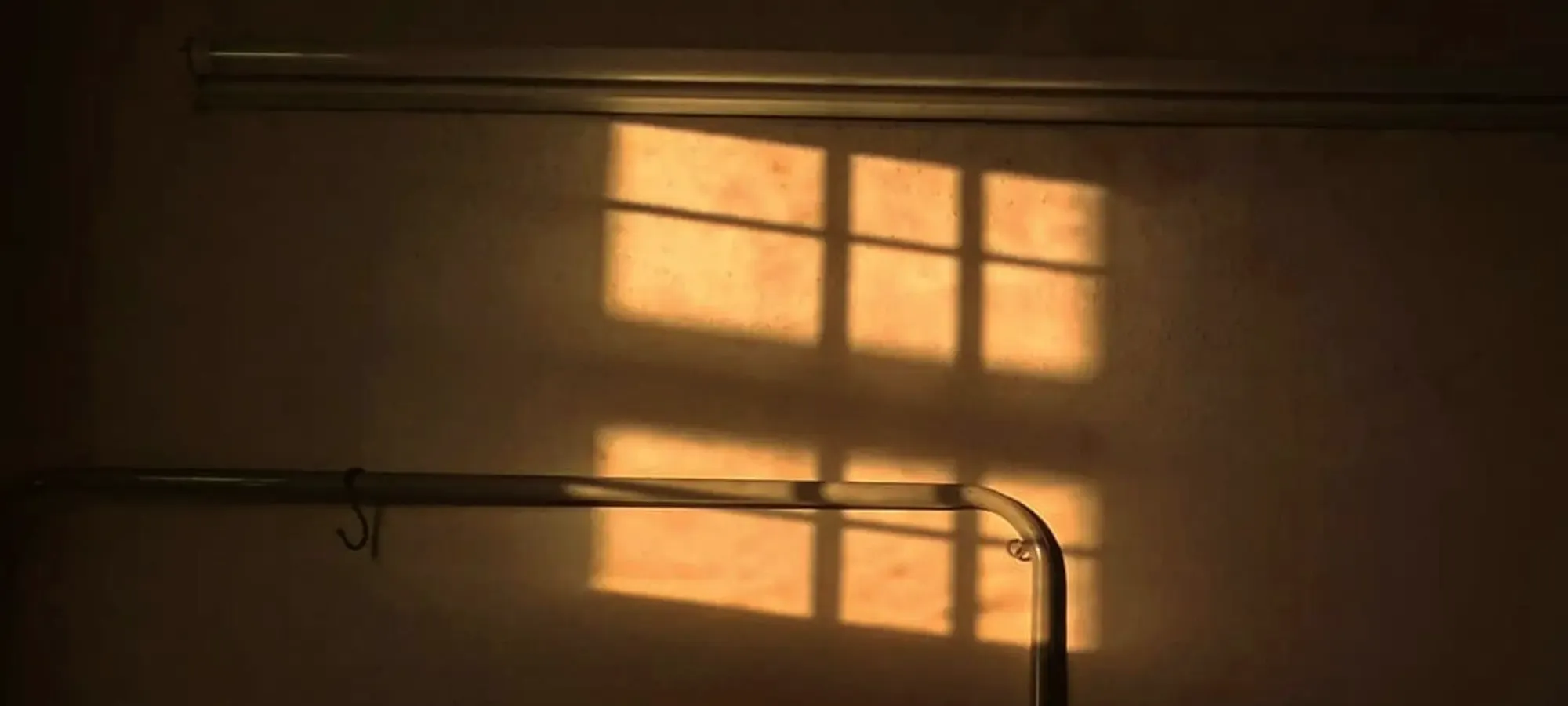 Später Sonnenschein wirft das Muster eines Fensters auf eine Wand.
